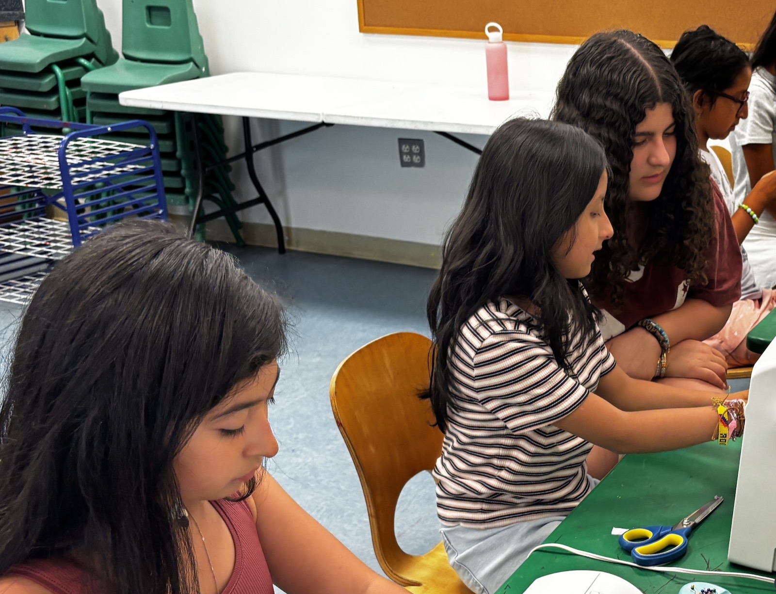 Two girls at a sewing machine on a green table in Montreal